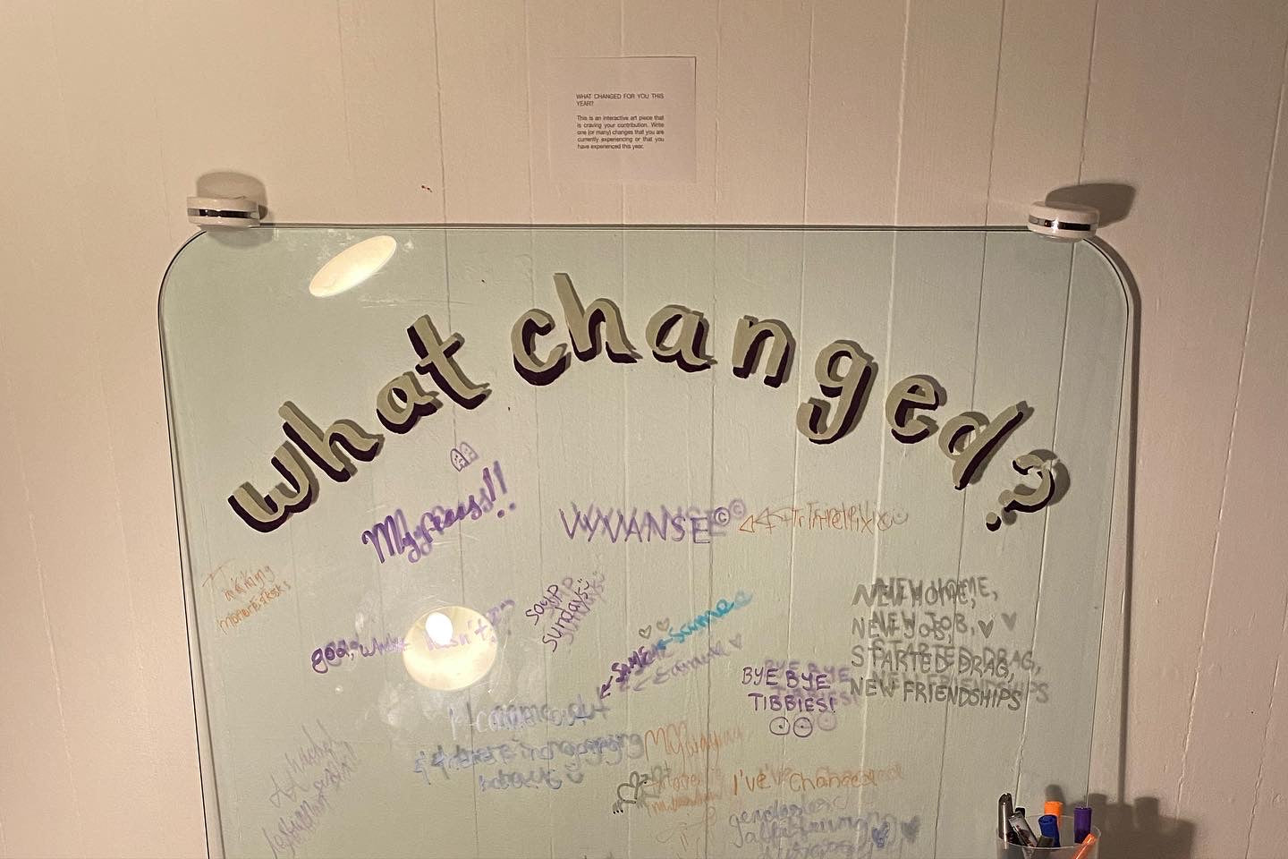The interactive art piece at the event is a large glass surface leaning against a wall, with the words "What changed?" painted on. Guests have used markers to write down things that changed for them in the past year and have filled up the glass surface.