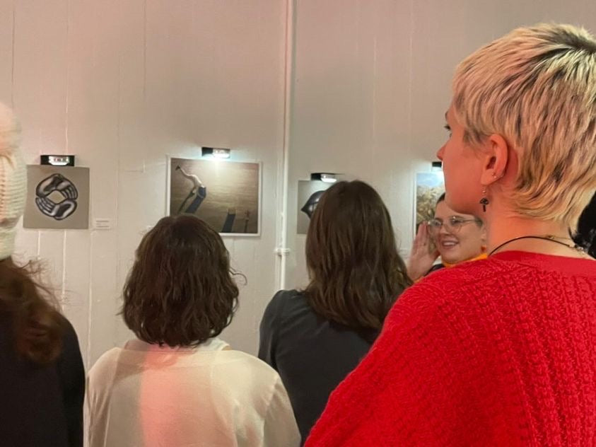 A crowd of people are facing away from the camera looking at the art on the wall