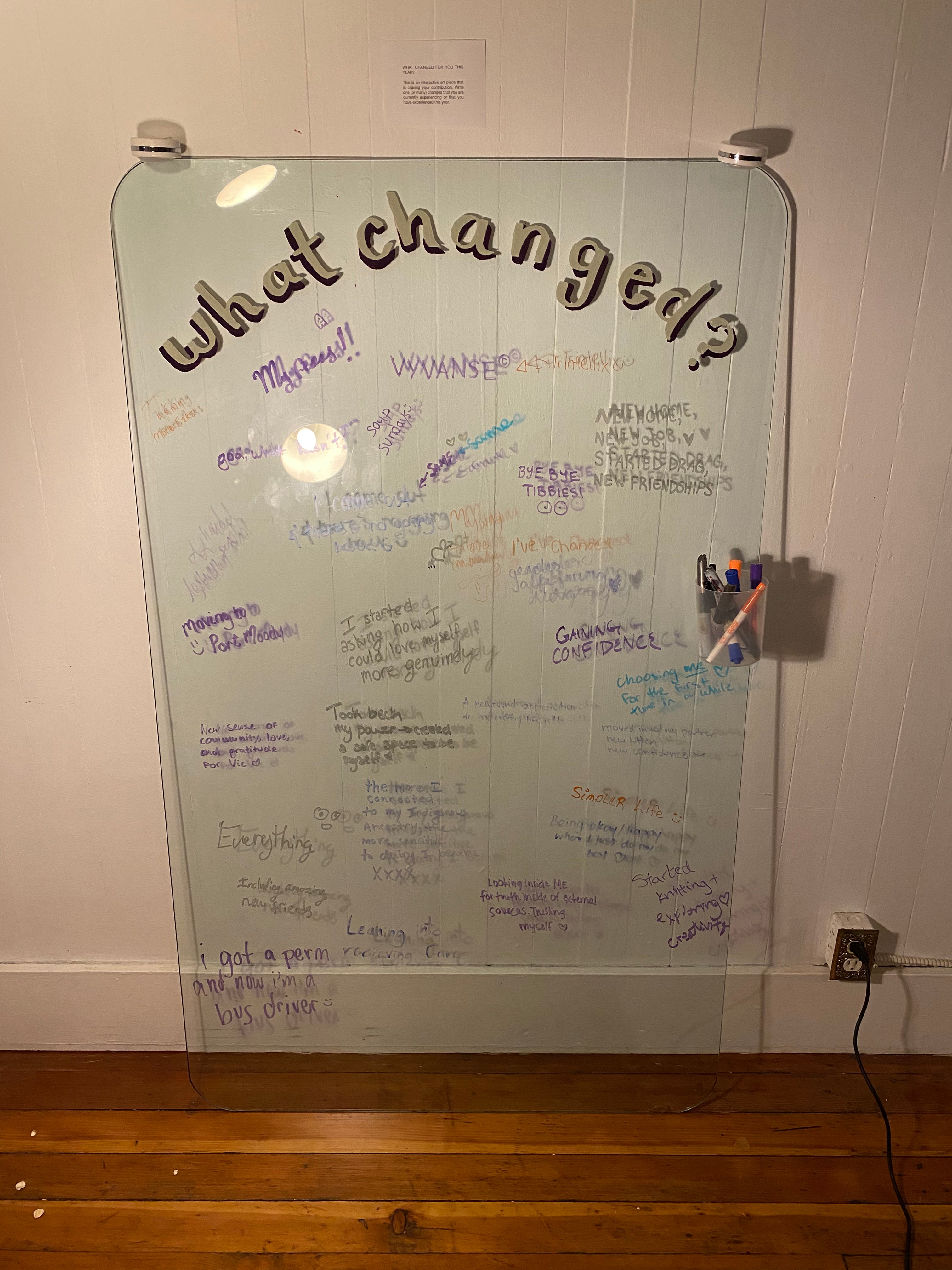 The interactive art piece at the event is a large glass surface leaning against a wall, with the words "What changed?" painted on. Guests have used markers to write down things that changed for them in the past year and have filled up the glass surface.
