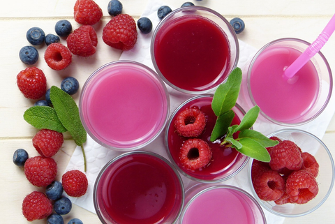 Several glasses of a fruity dessert with raspberries and blueberries on the side.