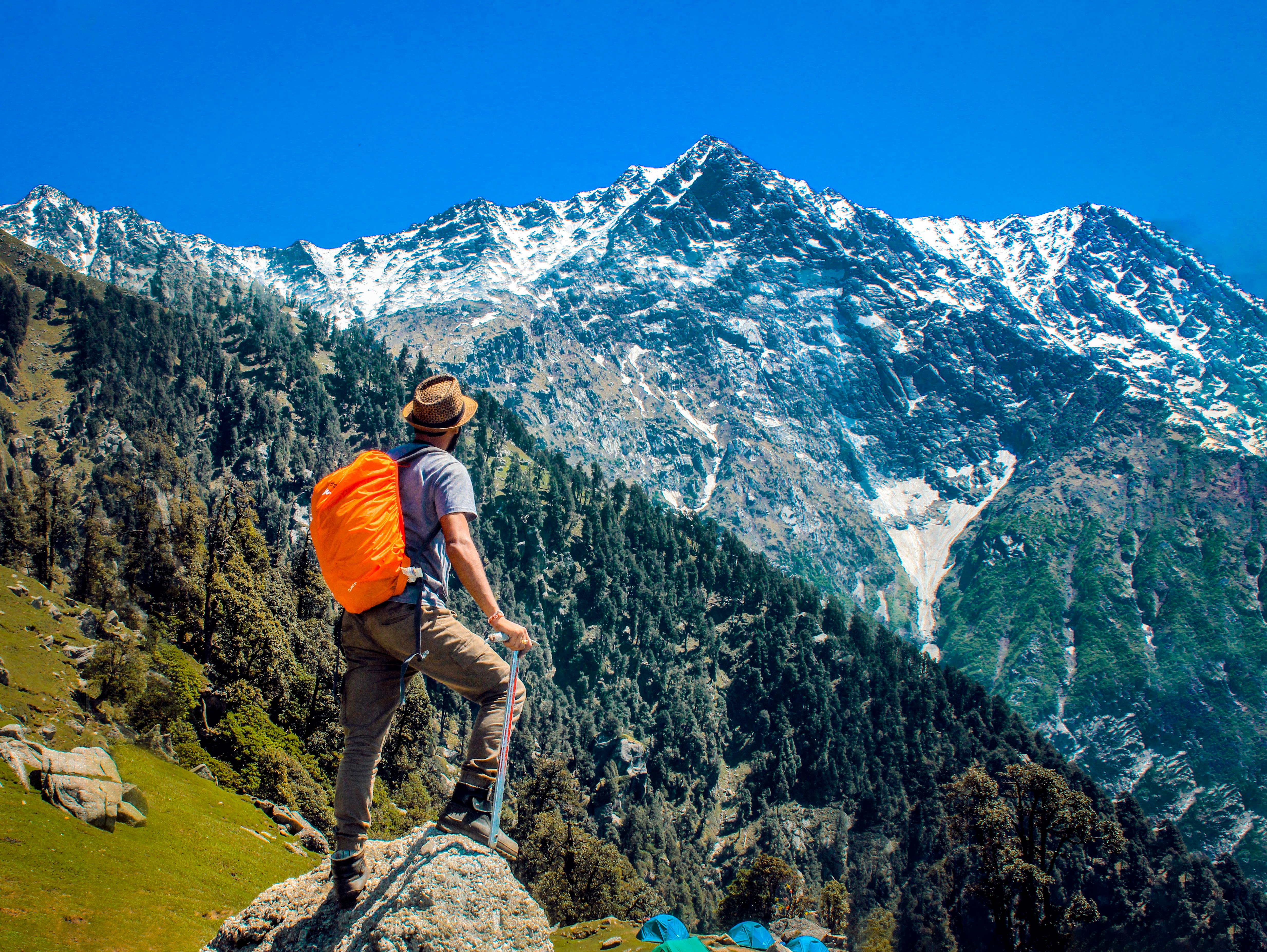 一个男人背着桔色背包眺望远处的山峰