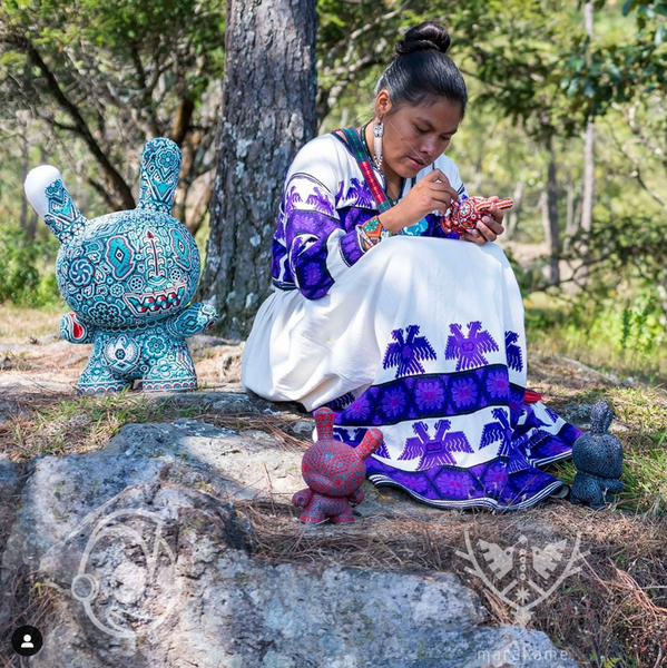 Mujer indígena huichol interviniendo con chaquira de cristal piezas de KidRobot Dunny y Munny. Al fondo hay árboles.