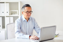A man sitting at his computer with reading glasses on
