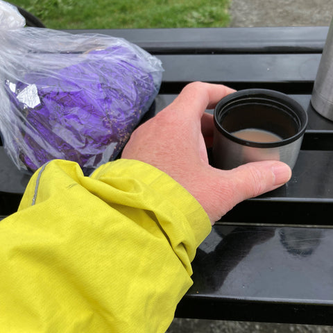 Arm and hand holding a cup of tea next to a bag of chocolate