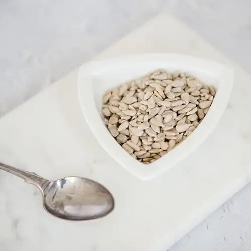 White bowl of sunflower seeds with teaspoon to the side