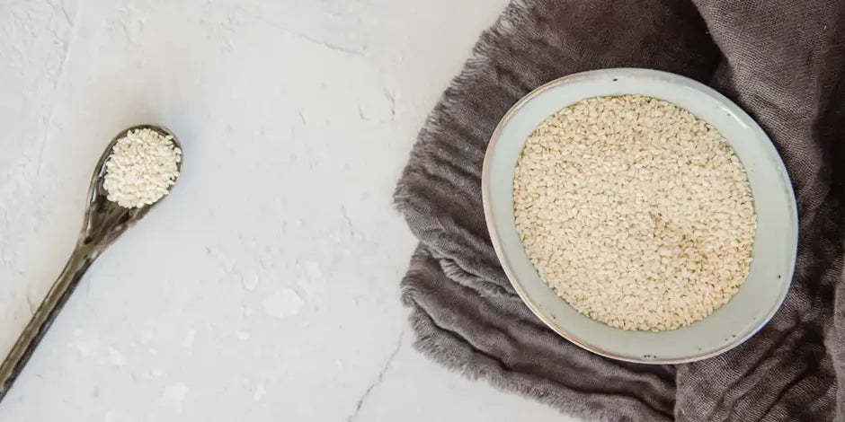 Bowl of sesame seeds on grey tea towel with grey spoon of sesame seeds