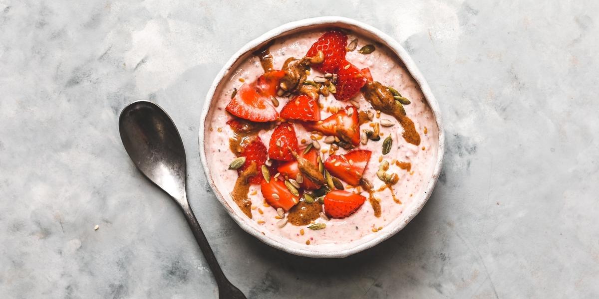 Fresh strawberries on top of a berry yoghurt bowl with spoon.