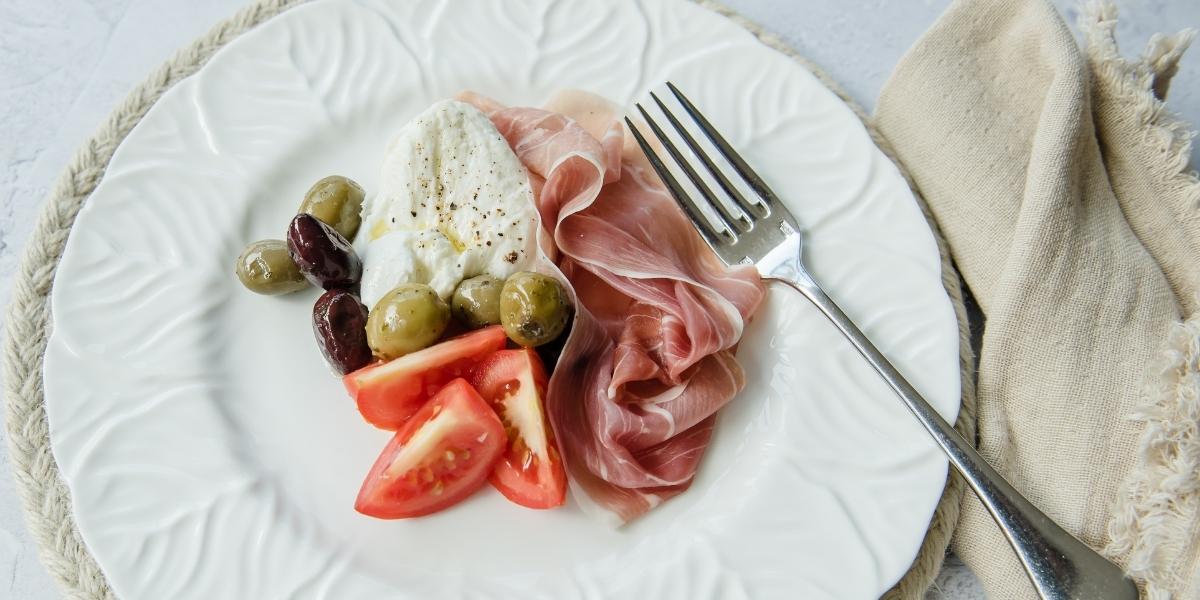 Plate of anti-pasti; green and black olives, tomato, buffalo mozzarella and prosciutto crudo. 