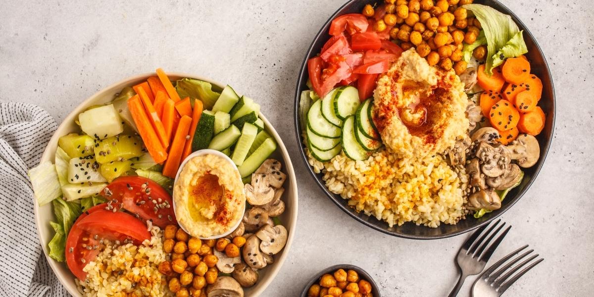Plates of food; 2 Vegan buddha bowls - Salads, chickpeas, houmous, veggie sticks, tomatoes and mushrooms.