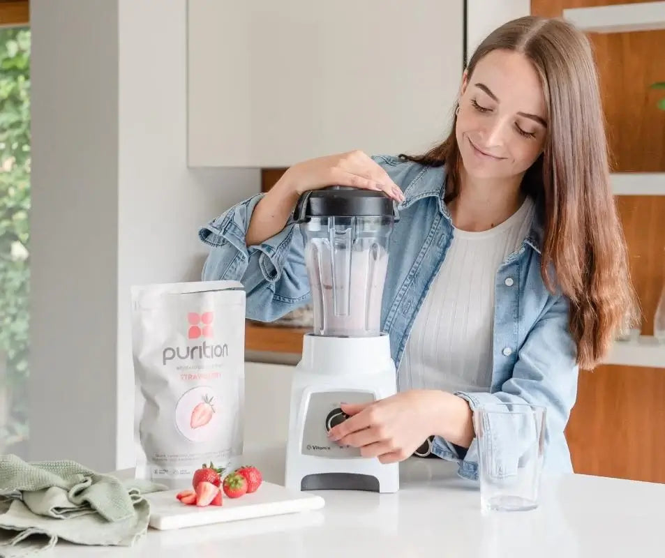 Smiley person blending a Purition Strawberry smoothie in the kitchen.