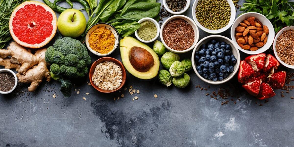 A tabletop display of natural foods; blueberries, ginger; almonds, oats, chia seeds, pomegranate, spinach and salad leaves.