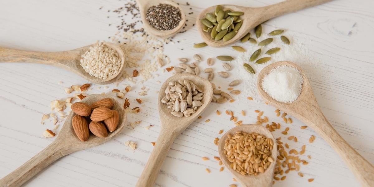 7 wooden spoons full of colourful seeds and nuts used to make Purition; sesame seeds, flaxseed, coconut, pumpkin seeds, chia seeds, almonds & sunflower kernels.