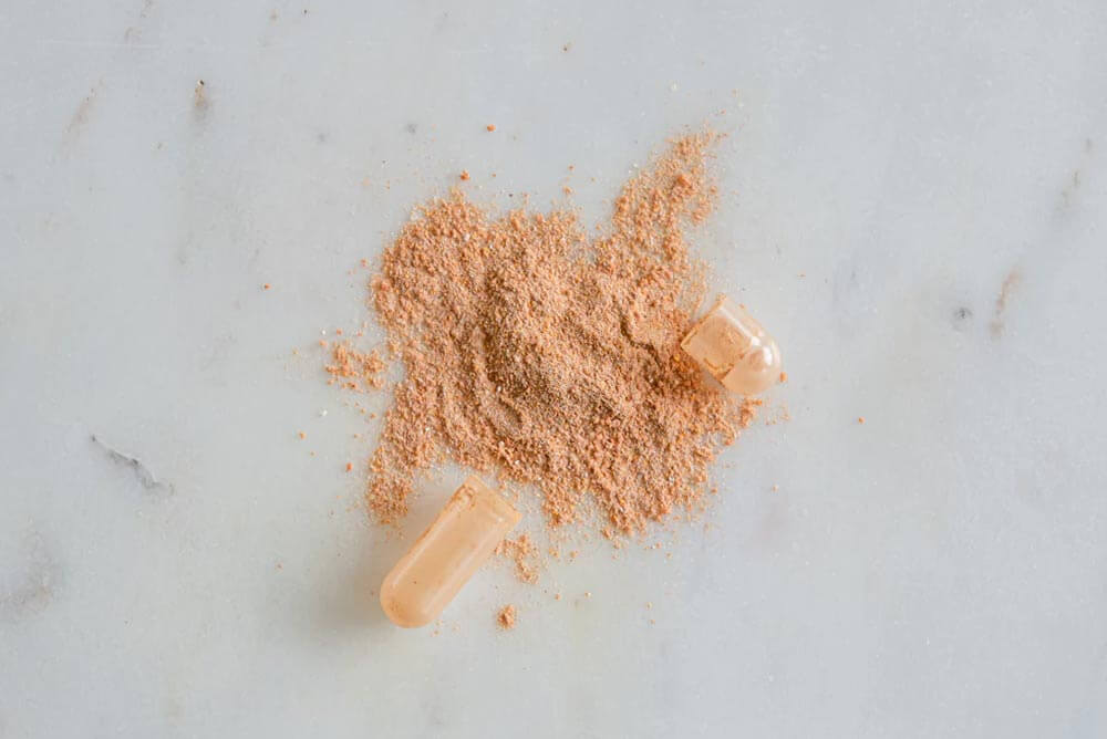 A Purition multi nutrient capsule opened up to expose content - a peachy coloured powder