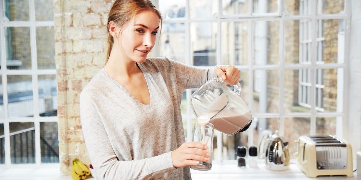 Woman in kitchen pouring smoothie from blender into cup