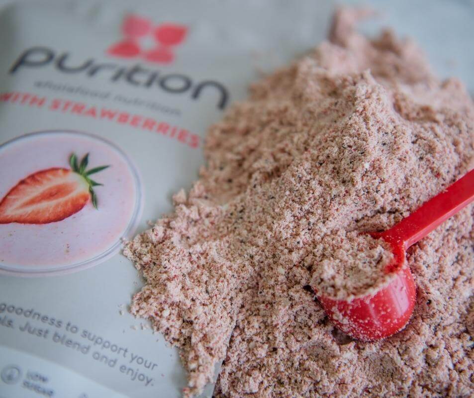 An open pack of Purition Strawberry with a pile of the natural product next to it and a red 10g measuring scoop.