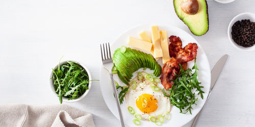 Keto-friendly meal plate of eggs, avocado, cheese, bacon and rocket