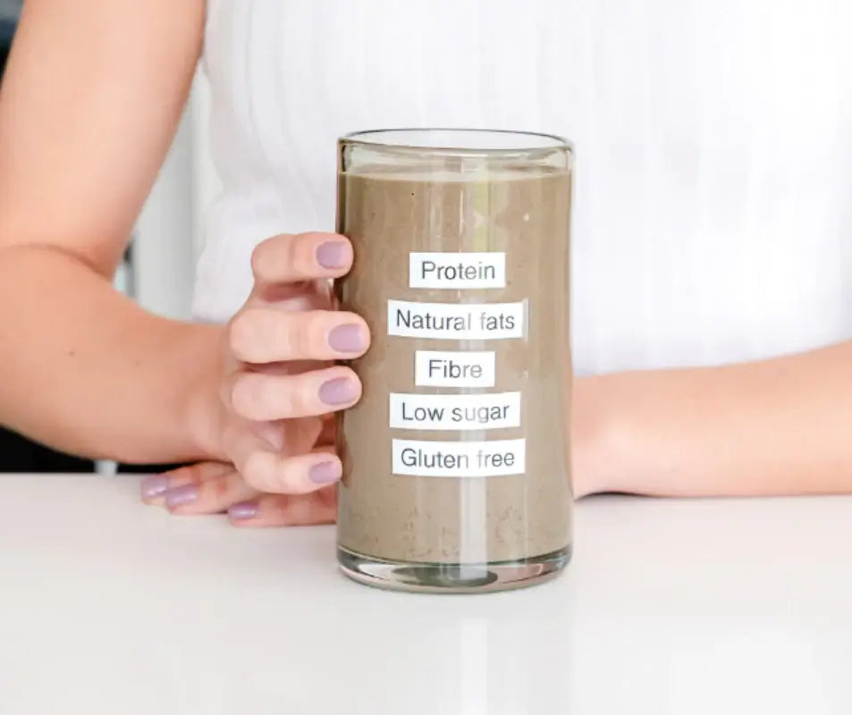 Person holding a glass of Purition with individual labels listing; Protein, Natural fats, Fibre, Low sugar and Gluten free.