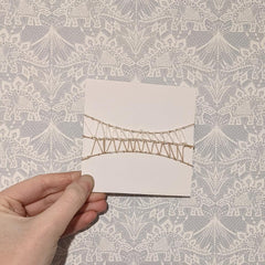 4 inch card horizontally wrapped with cream and ivory yarn, knotted and wrapped to create an hour glass shape.