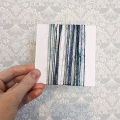 4 inch card vertically wrapped with a variety of blue and silver textured yarns.