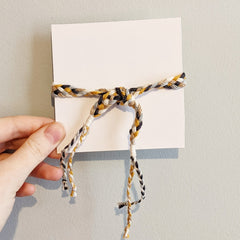 4inch card wrapped in braided yarn, colored yellow black and cream.