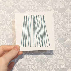 4 inch card punched with holes and woven with pale green yarn in v shapes.