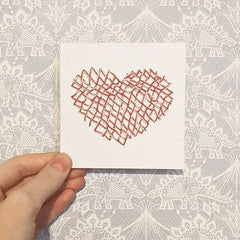 4 inch card punched with holes and cross stitched with pink and cream yarn in the shape of a heart.