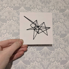 Card punched with holes and embroidered with black yarn in an abstract spikey shape.