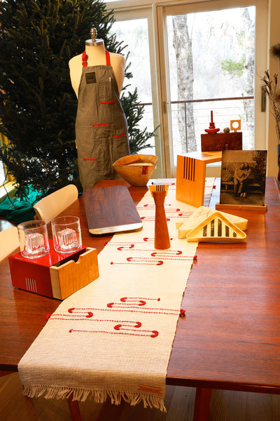 A photo of a table set with many hand crafted objects, including a table runner, set of cocktail glasses, cutting board, candle sticks and more.