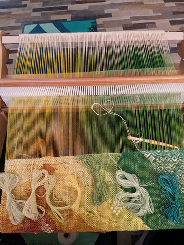 The warp on the loom has been shifted forward, now featuring the top half of the piece in orange, yellows and greens.