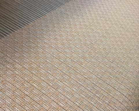 close up of cream and peach fabric on a loom.