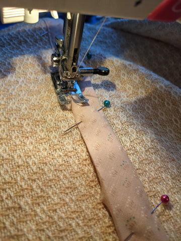 Image of fabric on a sewing machine, with bias tape pinned in place.