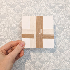 A 4 inch square card wrapped with overlapping strands of yarn in cream and tan.