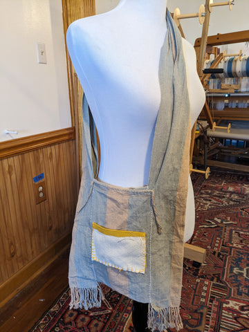 A unique canvas bag sits on the shoulder of a mannequin. A large fabric patch that is yellow and cream has been sewn onto the side of the bag creating a pocket.