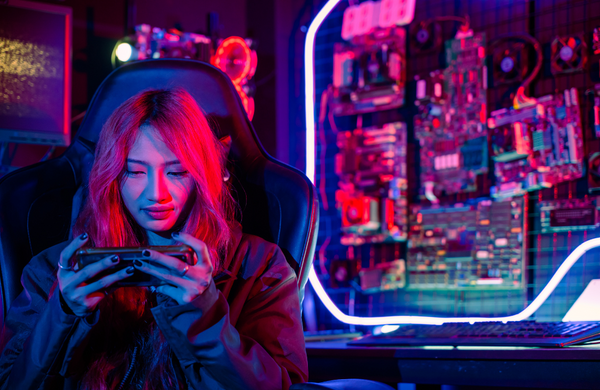 A girl sitting at her computer playing games on her phone.