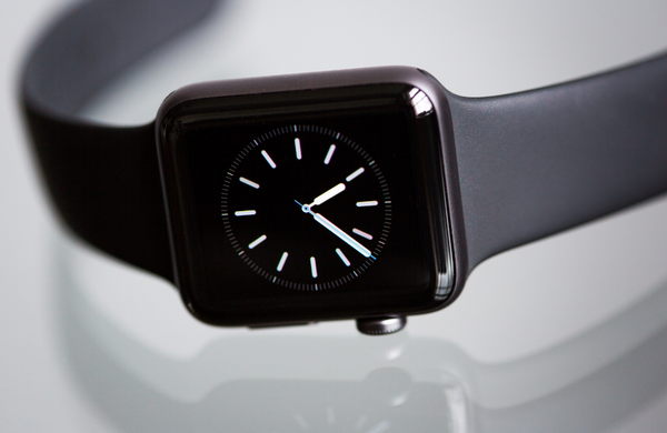 A close up of a titanium grey Apple Watch displaying the time on an analogue clock as 4:37