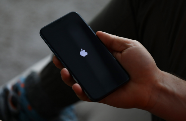 A hand holding an iPhone with a the Apple logo on the screen.