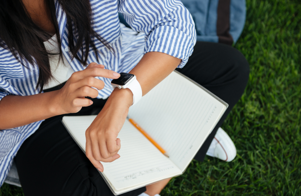 A woman sitting on grass checking her smartwatch while studying