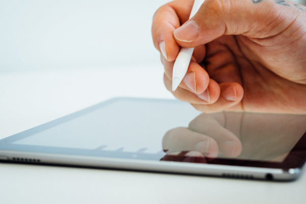 A hand hovering over a tablet holding the pen accessory.