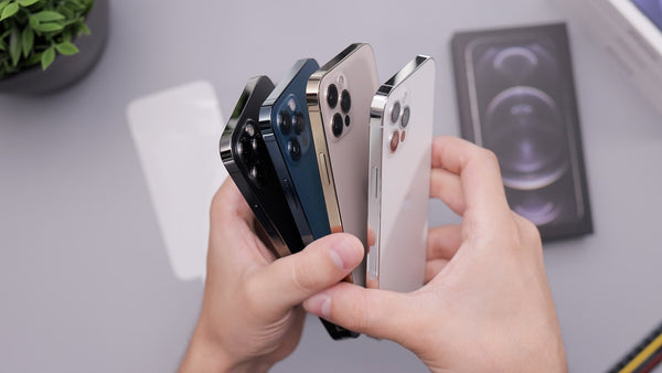Hands holding four different coloured iPhones