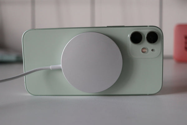 A green iPhone on its side attached to a MagSafe charger.