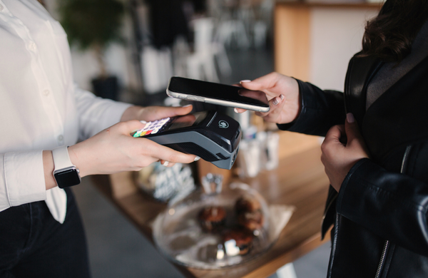 A server holding out an Eftpos machine with a person wearing a leather jacket holding their phone up to the machine to pay.