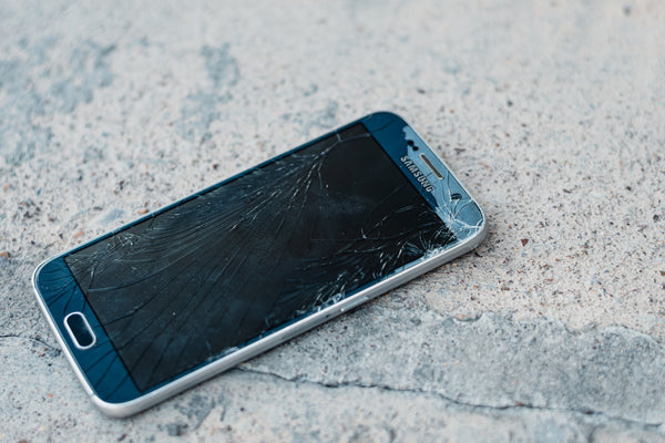 A Samsung smartphone on cement facing up with a smashed screen.