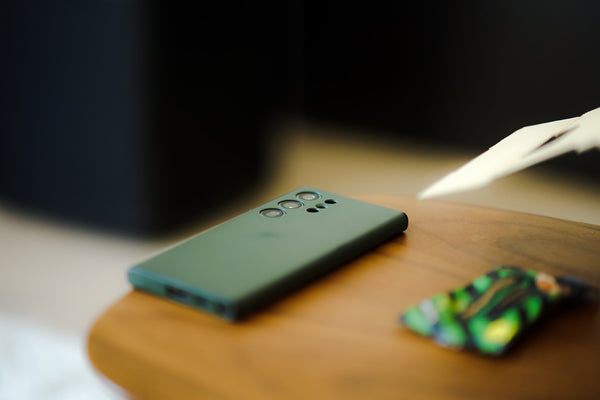 An army green Samsung smartphone face down on a wooden table