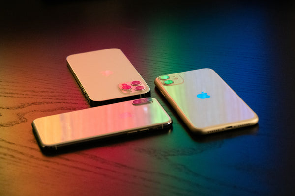 Three iPhones laying flat on wooden table with dark red, green and blue shadow