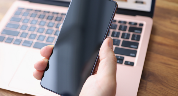 A hand hold a Samgsung smartphone over a pink laptop.