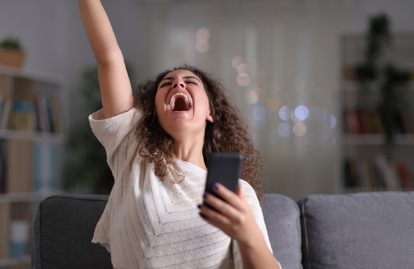 A woman holding a Samsung phone throwing her other arm up in excitement.
