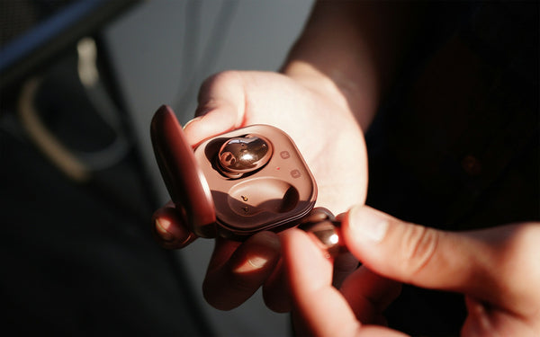 Two hands holding rose gold Samsung Galaxy buds