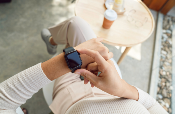 A woman sitting at a coffee shop pressing the button on her smartwatch.