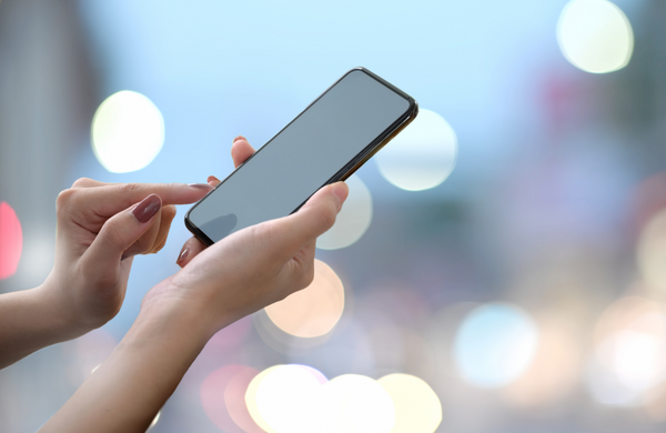 A woman's hands holding a phone with lights out of focus in the background.