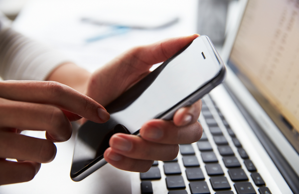 A person holding a phone with a black screen in front of their laptop. their finger is poised ready to press something on the screen.